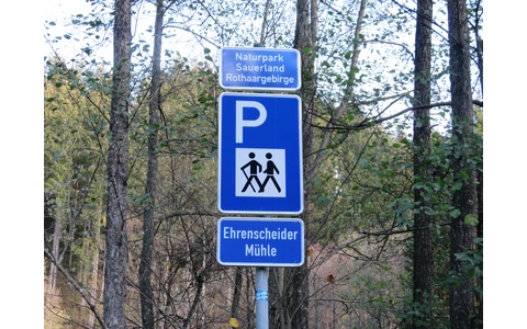 Blaues Schild für einen Wanderparkplatz mit einem weißen P und zwei wandernden Strichmännchen, sowie der Aufschrift Ehrenscheider Mühle.