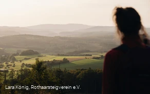Eine Frau blickt über die grüne, hügelige Landschaft am Rothaarsteig