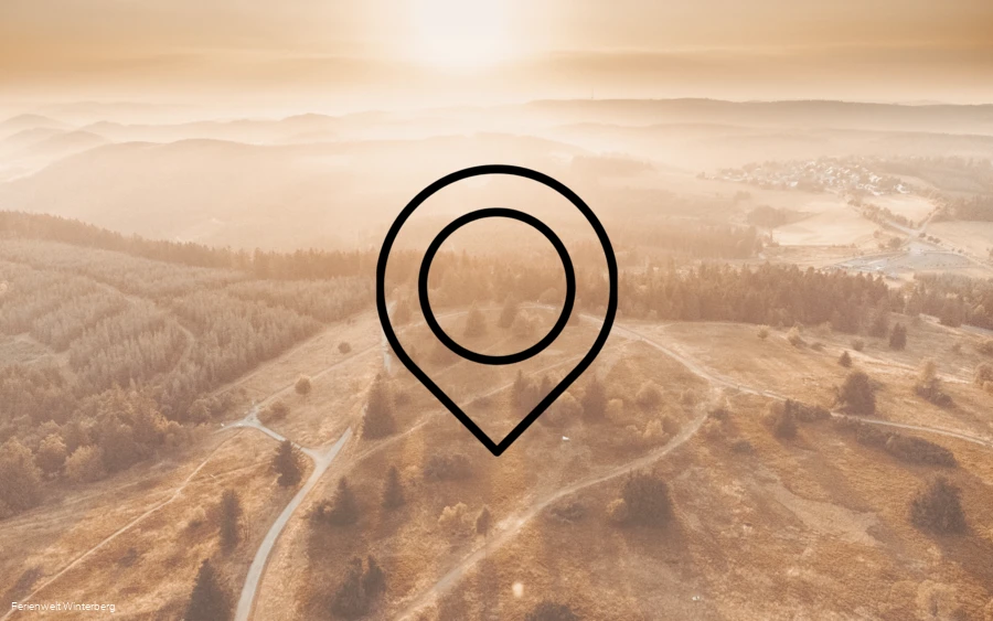 Drohnenaufnahme einer weitläufigen Landschaft aus Bergen, Wäldern und Wiesen mit der Zeichnung eines Markierungszeichens im Vordergrund. Dieses Bild dient als Symbolbild für Sehenswürdigkeiten.