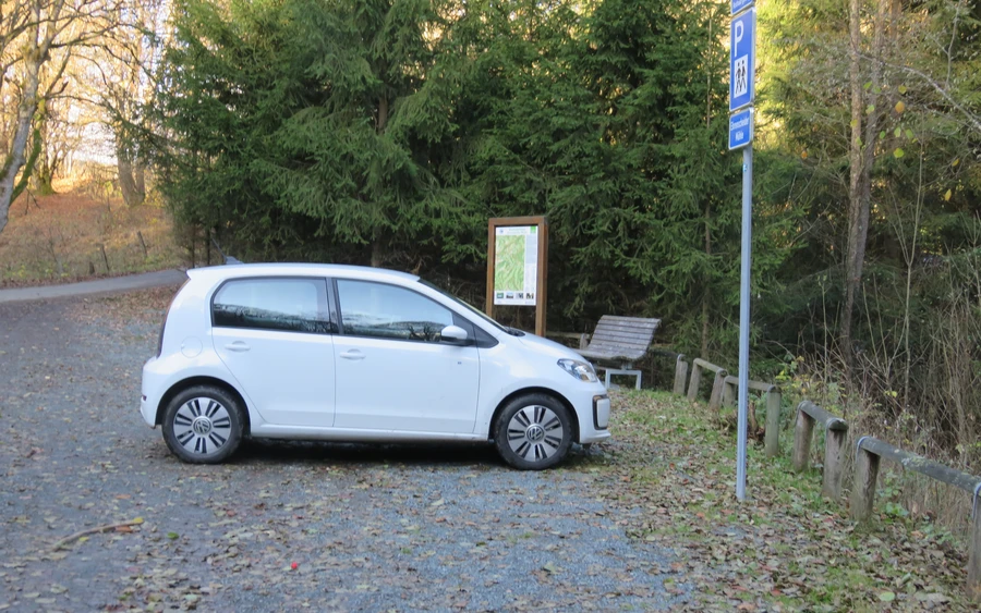 Kleines weißes Auto parkt auf Parkplatz im Wald.