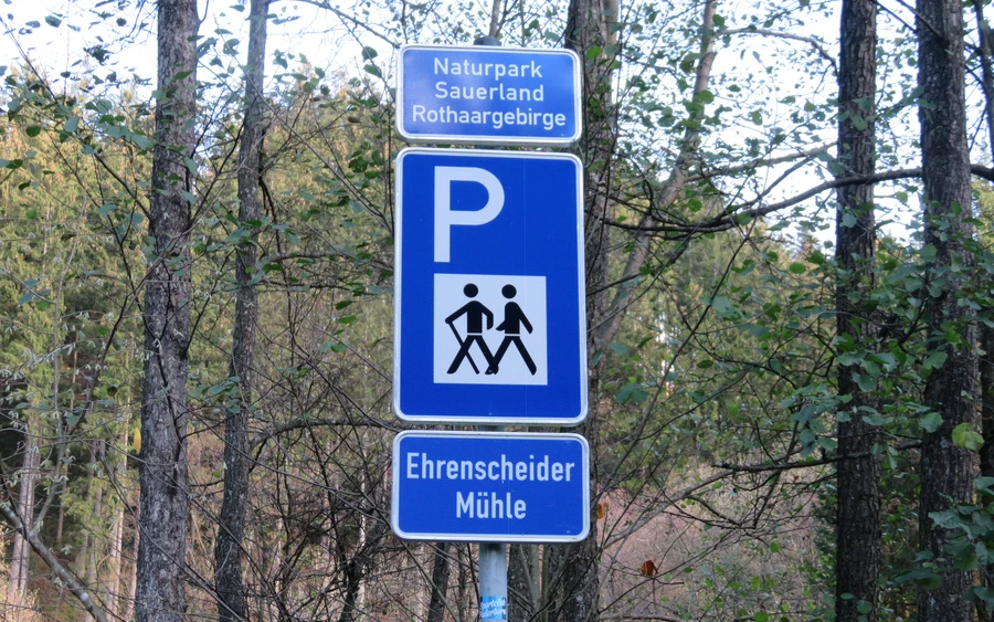 Blaues Schild für einen Wanderparkplatz mit einem weißen P und zwei wandernden Strichmännchen, sowie der Aufschrift Ehrenscheider Mühle.