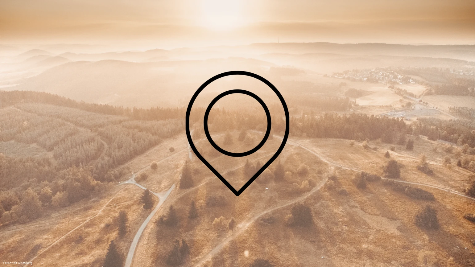 Drohnenaufnahme einer weitläufigen Landschaft aus Bergen, Wäldern und Wiesen mit der Zeichnung eines Markierungszeichens im Vordergrund. Dieses Bild dient als Symbolbild für Sehenswürdigkeiten.