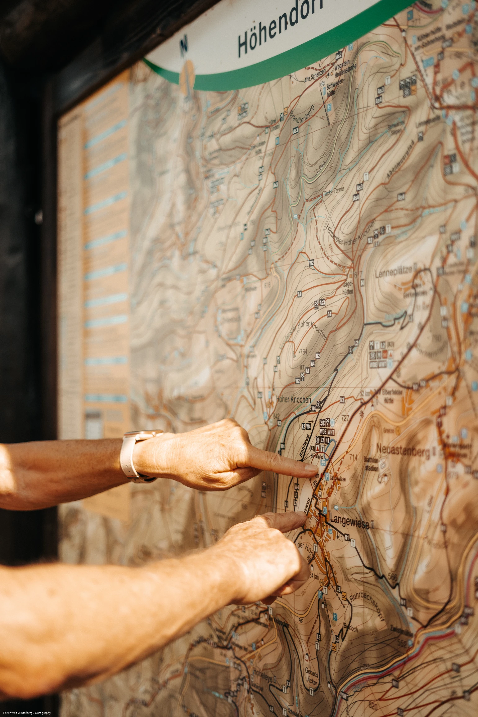 Zwei Hände, die mit dem Zeigefinger auf einer Wanderkarte auf etwas zeigen.