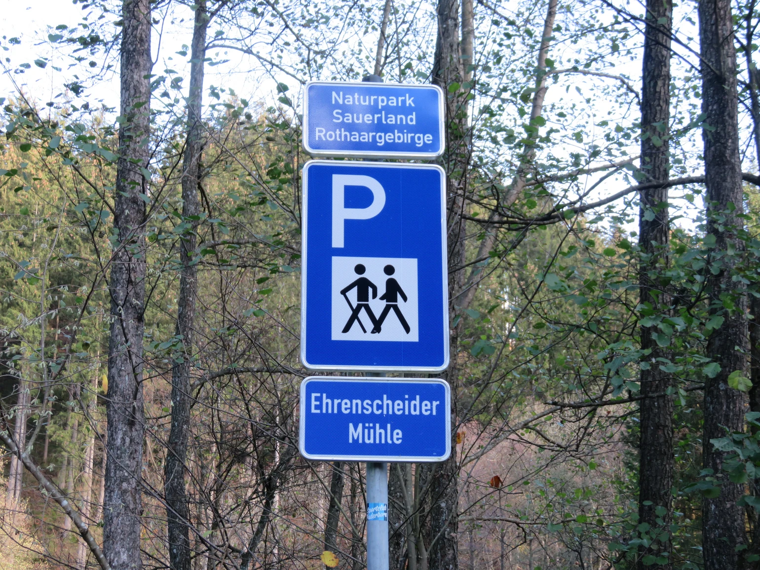 Blaues Schild für einen Wanderparkplatz mit einem weißen P und zwei wandernden Strichmännchen, sowie der Aufschrift Ehrenscheider Mühle.
